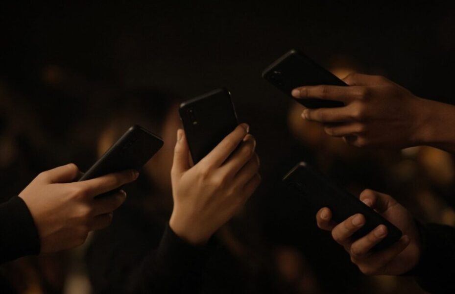 Kilka telefonów trzymanych w dłoniach, ekrany niewidoczne.
